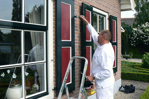 Een schilder van Vanderlaan schildert houten luiken